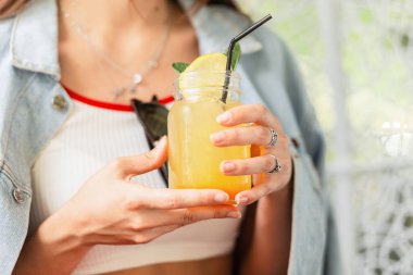 Nane yapraklı buzlu taze sıkılmış limon-portakal suyu. Elinde narenciye ve limonata bardağı tutan bir kadın. Yakın plan..