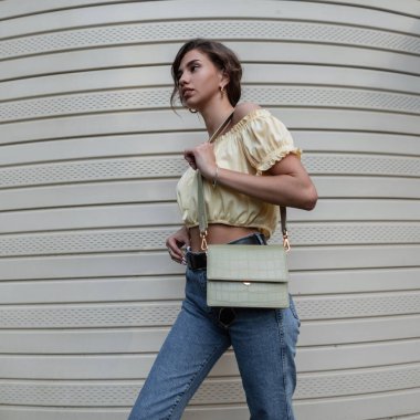 Moda kot giyen, deri çantalı, şık, kıvırcık, çekici, hippi kız caddedeki klasik yan duvarın yanında yürüyor..