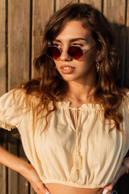 Moda modasına uygun güneş gözlüklü genç bir kadın. Gün batımında kumsalda sarı bir bluz.