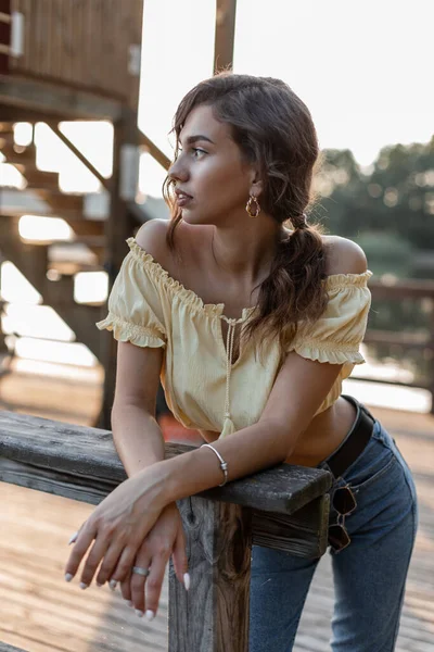美しいです巻き女性でデニム服で夏の黄色のトップブラウスとジーンズスタンドと木製の桟橋に残ります — ストック写真