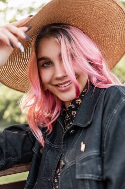 Güzellik portresi çekici gülümseyen pembe saçlı, güzel gözlü, şık kot ceketli, açık havada şık şapkalı genç bir kadın. Şirin, pozitif, tatlı gülüşlü kız modeli..