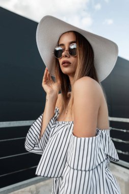Çok şık bir yaz elbisesi içinde, modaya uygun güneş gözlüklü, klasik hasır şapkalı, seksi dudaklı, açık havada poz veren bir kadın. Açık havada şık giyinen çekici Avrupalı kız.
