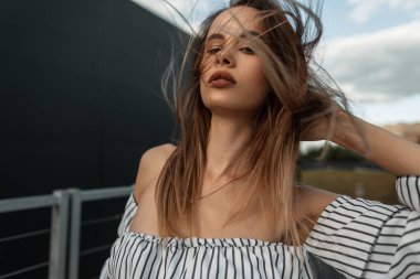 Nefis, şehvetli, genç bir kadın. Güzel dudakları, bronzlaşmış, sağlıklı bir teni, şık bir gömleği var. Rüzgarlı bir günde sokakta sırada bekliyor. Açık havada çekici, modaya uygun bir kız modeli..