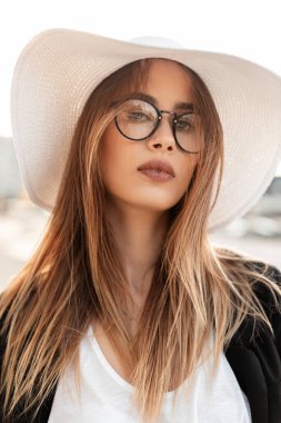 Güzel bir portre. Temiz, narin tenli, kahverengi saçlı, seksi dudaklı, moda gözlüklü, beyaz bluzlu, saman şapkalı, açık havada güneşli bir günde siyah ceketli güzel bir kadın. Zarif bir bayan..