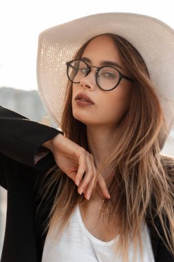 Moda gözlüklü, şık hasır şapkalı, şık siyah şık ceketli şık bir bayan model sokakta poz veriyor. Taze portre. Güzel kız. Moda kıyafetleri içinde..