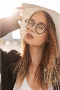 Güneşli bir günde, şık hasır şapkalı, siyah, şık spor ceketli, klasik gözlüklü, Avrupalı şık bir bayan. Vogue portresi yaz güneşinin altında güzel bir kız..