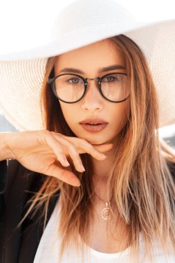 Sevimli, genç, güzel, seksi dudakları olan, harika gözleri olan, modaya uygun siyah ceketli, şık şapkalı, açık havada güneş ışığından hoşlanan genç bir kadın. Güneşli bir günde sokakta güzel bir kız portresi.