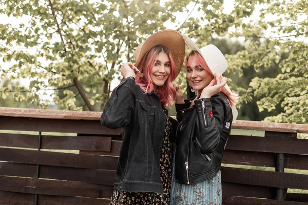 时尚快乐的妹妹们穿着时尚的青春夏装 穿着新系列的草编时髦帽子 站在户外老式木制篱笆边 快乐的女朋友在农村休息 — 图库照片