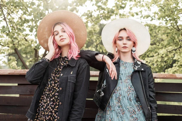 两个性感的年轻女子穿着时尚的青春夏装 头戴草编时髦帽子 站在城外老式木制篱笆旁边 迷人的时髦女友在大自然中休息 — 图库照片