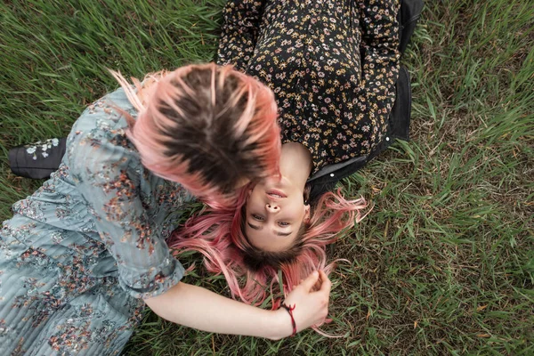 两个穿着时髦夏装 一头粉色时髦头发的年轻貌美的女同性恋者躺在城外田野里鲜绿的草地上 迷人优雅的女朋友们在户外放松一下 顶部视图 — 图库照片
