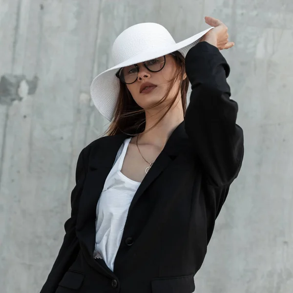 ファッショナブルなセクシーな若い女性でビジネスファッショナブルな黒 白の服でスタイリッシュなメガネストレートファッションわら帽子でグレーの背景屋外 — ストック写真