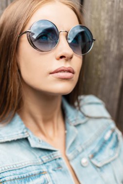 Beyaz yüzlü, şık, yuvarlak güneş gözlüklü, açık havada kot ceket giyen güzel bir kadının moda portresi.