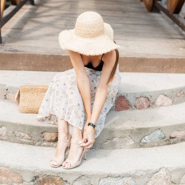 Sahil hasır şapkalı, şık dantelli iç çamaşırlı ve el çantalı, klasik etekli güzel bir kız ayakkabısını giyer.