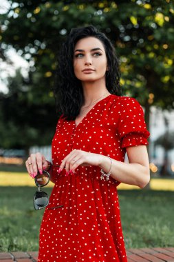 Kıvırcık saçlı, kırmızı elbiseli güzel bir kadın parkta yürüyor.