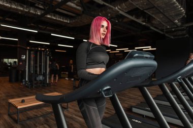 Spor salonunda koşu bandında koşan şık siyah spor kıyafetleri olan güzel genç bir kadın.