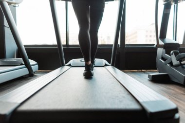 Spor kıyafetleri ve spor ayakkabıları olan genç bir kadın spor salonunda koşu bandında koşuyor.