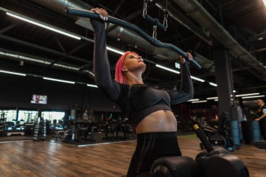 Siyah eşofmanlı güçlü kız spor salonunda oturur ve egzersiz yapar.