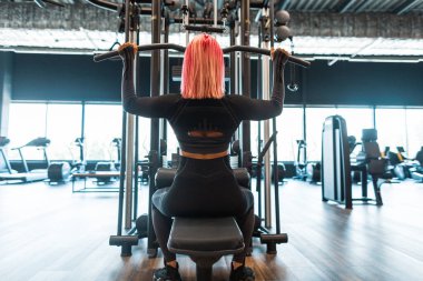 Güzel bir fitness kadını, siyah spor kıyafetleri içinde spor salonunda egzersiz yapıyor, arkadan bakıyor.