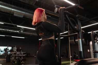 Siyah spor kıyafetli güzel bir kadın spor salonunda egzersiz yapıyor ve kaslarını çalıştırıyor.