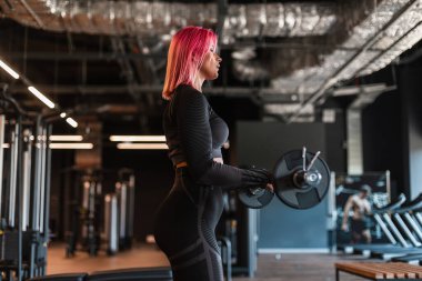 İnce vücutlu havalı atletik genç sağlıklı kız ve siyah spor giyimli pembe saçlar spor yapıyor ve salonda, yan görüşte egzersiz yapıyor.