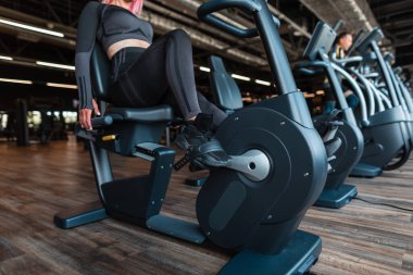Spor kıyafetli spor ayakkabılı kadın spor salonunda sabit bisikletli tren kullanıyor.
