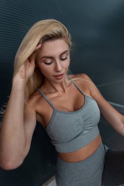 Beyaz tenli, gri spor giyimli, açık hava arka planında spor kıyafetli, mutlu beyaz kadın portresi.