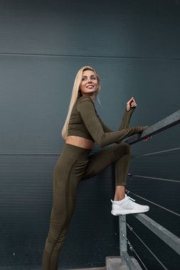 Moda yeşili spor giyimli, beyaz spor ayakkabılı güzel fitness kızı şehirde duruyor.