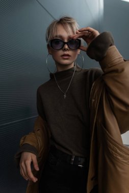 Modern bir şehirde, şık güneş gözlüklü, deri ceketli ve süveterli güzel bir kız.