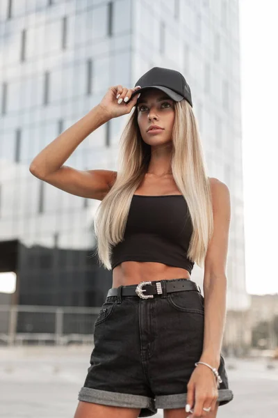 时尚美女穿着黑色时髦T恤和黑色牛仔裤短裤 头戴一顶帽子在城里散步 — 图库照片