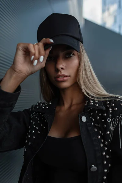 Moda mujer joven y bonita con un hermoso cuerpo atlético en una camiseta  negra con una gorra negra para maqueta de diseño en jeans negros se  encuentra en la ciudad