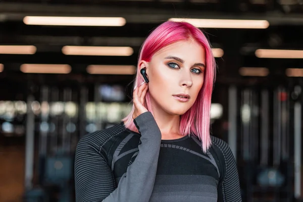 スポーツジムで働くワイヤレスヘッドフォンとピンクの髪とスポーティーな美しい女性モデルの肖像画 — ストック写真