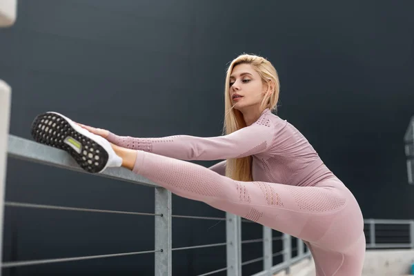 スニーカーでスポーティなスポーツウェア姿のフィットネスモデル女性が街中でストレッチ運動をする — ストック写真