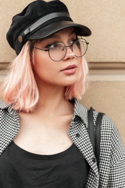 Şehrin duvarına yakın bir yerde klasik gözlüklü ve şapkalı genç bir kız modelinin sıradan moda portresi.