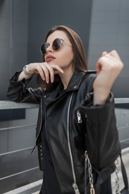 Hippi modasına uygun, modaya uygun güneş gözlüklü, şık siyah deri ceketli, şık havalı çanta taşıyan güzel bir kız şehirde yürüyor.