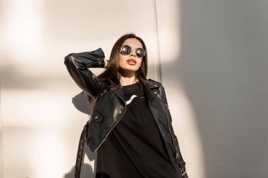 Havalı, güzel yüzlü, büyük seksi dudaklı, modaya uygun siyah deri ceketli ve şık güneş gözlüklü bir kadın.