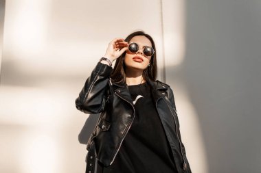 Moda modası geçmiş, siyah elbiseli, şık deri ceketli hippi bir kadın güneş gözlüğünden şehre bakıyor.
