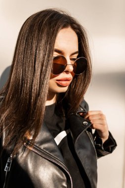 Şafak vakti şehirde, şık siyah elbiseli, deri ceketli ve eski moda güneş gözlüklü güzel ve çekici kız modelinin şehir portresi.