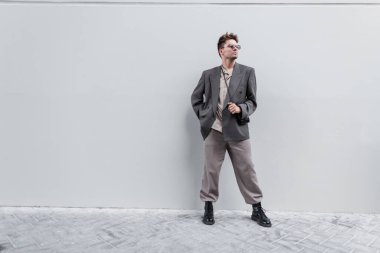 Şık, sıradan görünümlü, gömlekli, ceketli, pantolonlu ve botlu yakışıklı bir adam şehirde gri bir duvarın yanında duruyor. Metin ve logo için boş alan