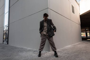 Moda kıyafetleri içinde şık, yakışıklı bir adam şehrin gri duvarının yanında poz veriyor. Erkek tarzı ve şehir modası