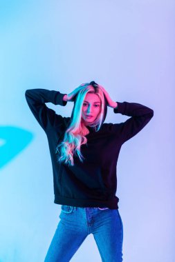 Şık, alımlı, çekici, siyah tişörtlü genç bir kadın. Stüdyoda mavi kot pantolonlu bir kapüşon giyiyor.