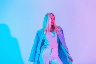 Stüdyoda mavi ceketli, beyaz kotlu ve neon pembe pastel ışıklı tişörtlü şık bir iş kadını. Yaratıcı renkli kadın portresi