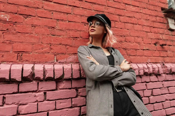 时尚漂亮的时髦姑娘 戴着眼镜 头戴便衣 头戴安全帽 站在古老的砖墙旁边 — 图库照片