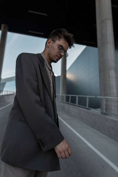 Молодой красивый модель парень в винтажных золотых солнцезащитных очках в модном сером костюме прогулки по городу