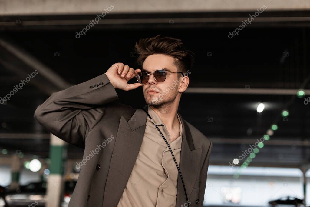 Handsome young business man with hairstyle in fashionable clothes look straightens sunglasses and walks on the street. Male casual style and fashion