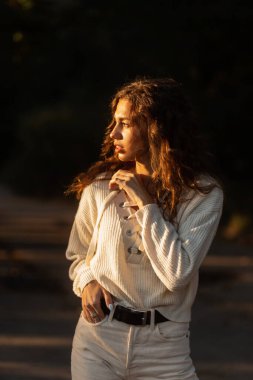 Şık örgü süveter giyen güzel kıvırcık kadın model gün batımında dışarı çıkıyor.