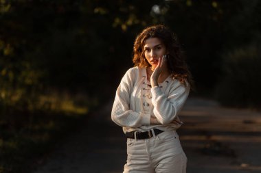 Şık, kıvırcık saçlı, şık örgü bluzlu güzel bir kadın. Gün batımında parkta.