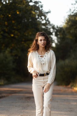 Kıvırcık saçlı, moda örgü süveterli güzel bir manken parkta yürüyor.