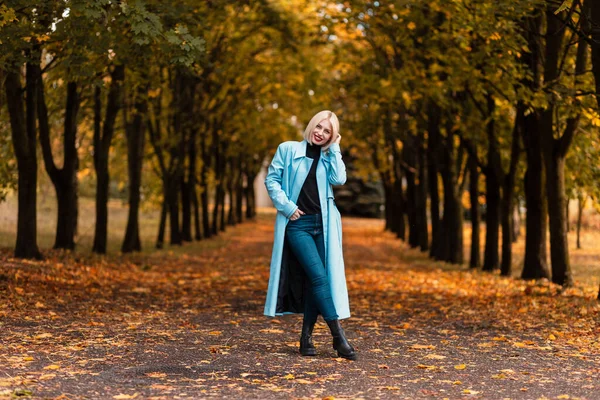 穿着时髦秋装的美丽微笑的女孩 穿着一件外套 走在公园里 绿叶飘落 — 图库照片