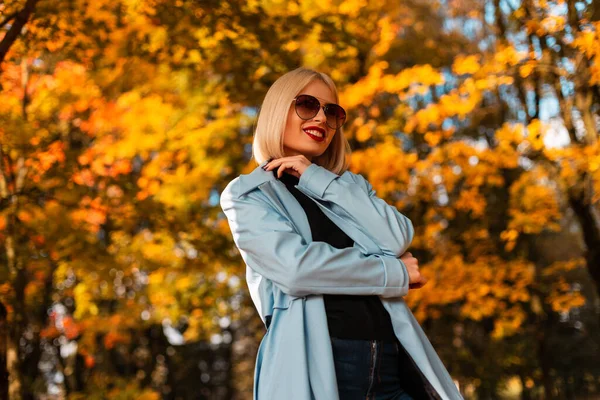 戴着太阳镜 头戴时髦服装 面带微笑的快乐的商界女性正在公园里走着 她的秋叶光彩夺目 — 图库照片