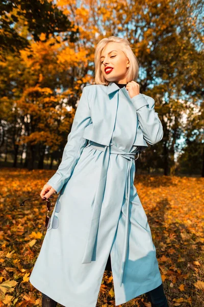 黄色の葉を持つ秋の公園でファッショナブルな青いコートの散歩とエレガントな美しい女性モデル — ストック写真